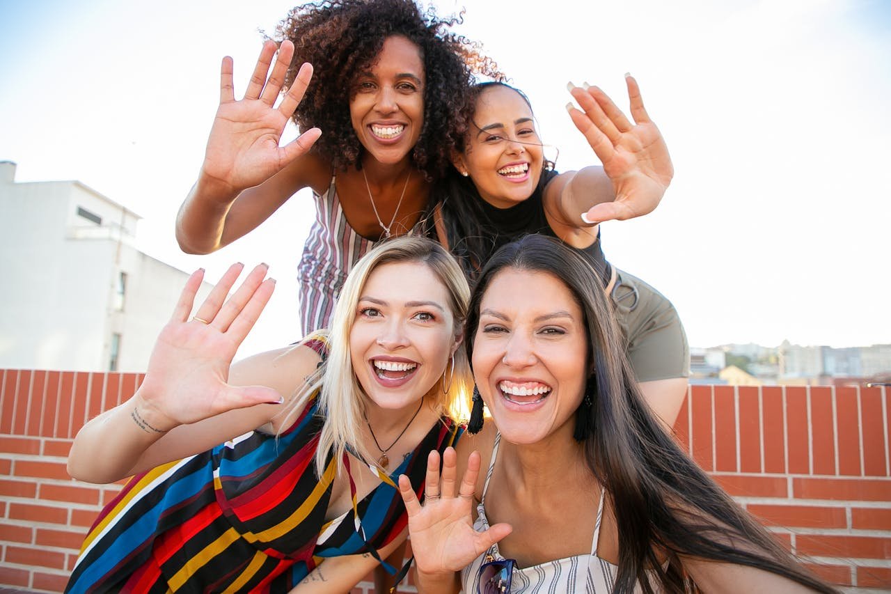 Photo by Kampus Production: https://www.pexels.com/photo/smiling-young-diverse-ladies-showing-hi-sign-while-taking-selfie-on-terrace-5935239/